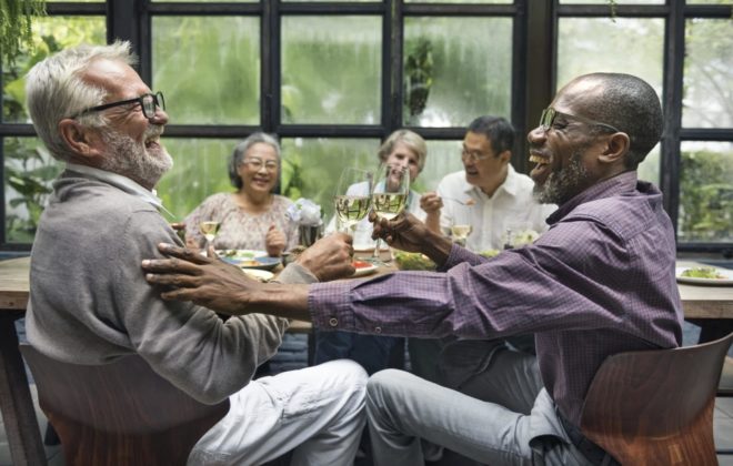 An older group of people laughing around the table discussing hearing health in New Jersey. 