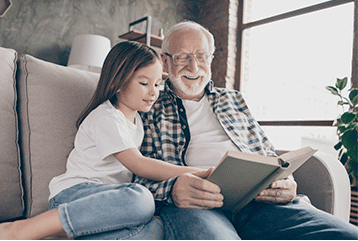 An older man with hearing impairment reading to his granddaughter in New Jersey. 