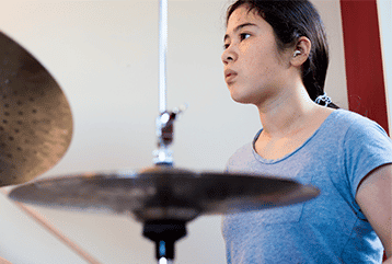 A young woman wearing hearing protection playing the drums in New Jersey. 