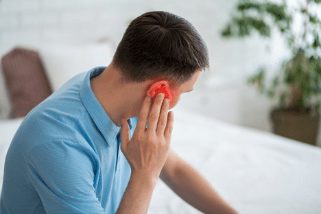 A man holds his ear due to ear pain highlighted in red for emphasis